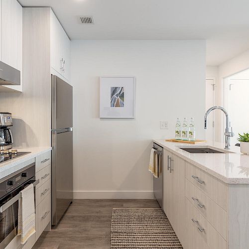 A modern kitchen with white cabinetry, stainless steel appliances, a coffee maker, a stove, a refrigerator, a sink, and minimalist decor, ending the sentence.