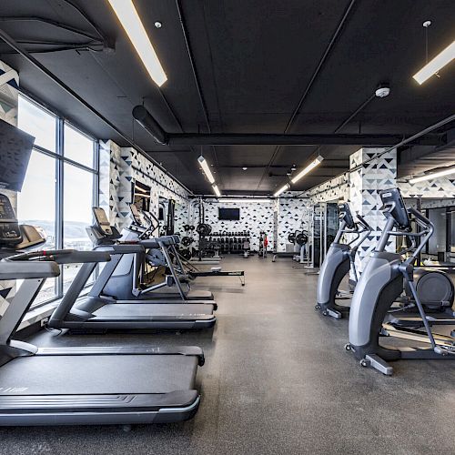 A modern gym with treadmills, elliptical machines, weights, and geometric wall designs is shown in the image.