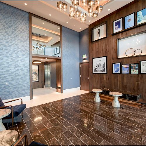 A modern lobby area with sleek black marble flooring, blue and wood-paneled walls, contemporary furniture, wall art, a chandelier, and an elevator.