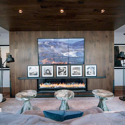 A modern living room with a fireplace below a wall-mounted TV, framed pictures, stylish furniture, and unique decor items.