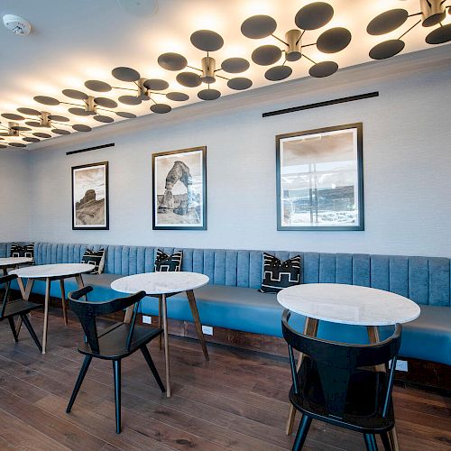 A modern room with blue seating, round tables, black chairs, wall art, and a decorative ceiling with circular elements ends the sentence.