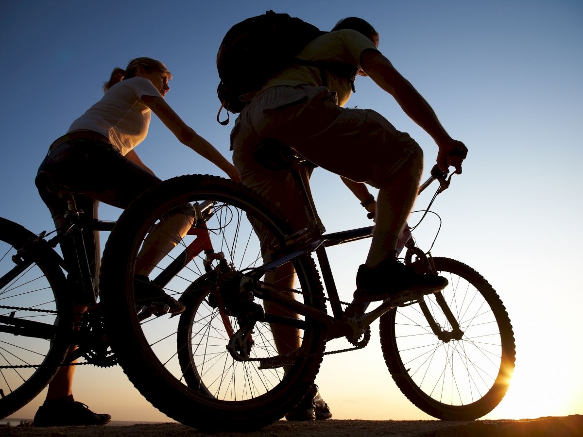 Two people are riding bicycles at sunset, silhouetted against the sky.
